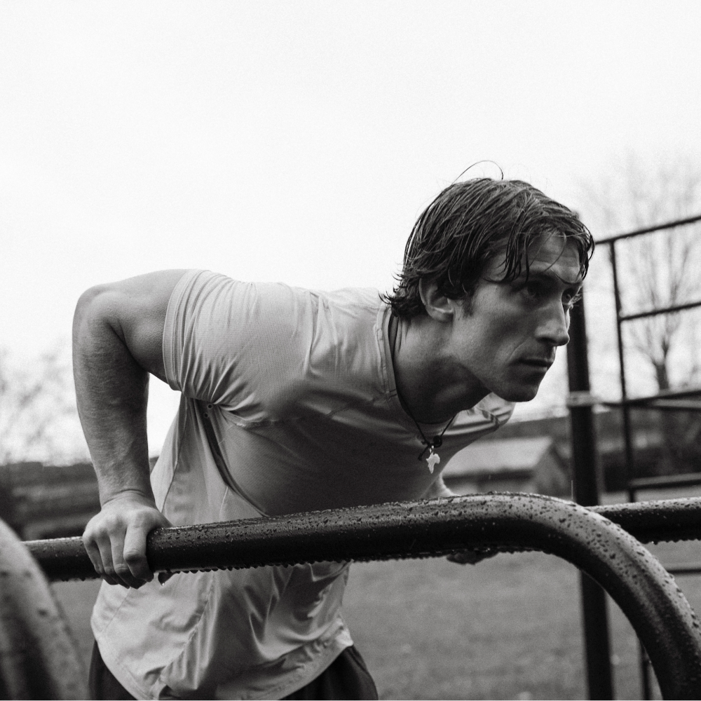 Alfie Cain doing push-ups on a playground bar with trees and playground equipment in the background